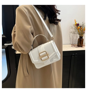 Detail of a white leather crossbody bag with a gold square buckle on a khaki coat
