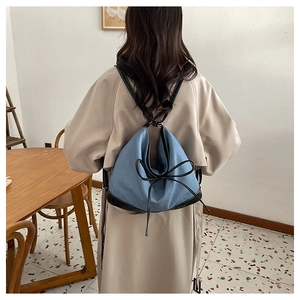 Blue denim backpack with black leather trim and bow detail worn by model at home
