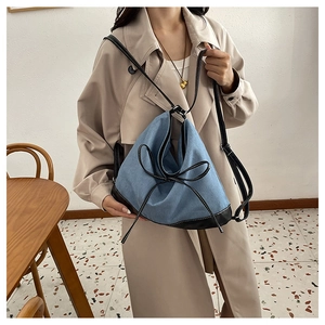 Detail of blue denim tote bag with black PU trim and decorative bow on the front