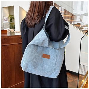 Detail view of light blue denim tote bag with textured wash and brown leather logo patch