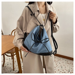Detail of a blue denim and black leather patchwork bucket bag with a bow accent