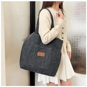 Detail of dark grey corduroy tote bag featuring a leather brand patch and long handles