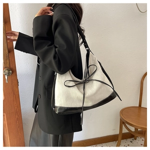 Large cream and black canvas tote bag with bow detail worn by model in black suit