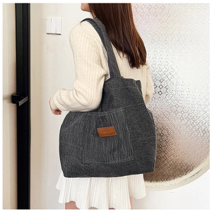 Detail of dark grey corduroy shoulder bag with brown leather label on model