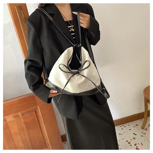 Detail view of canvas tote bag featuring contrast leather trim and woven bow accent