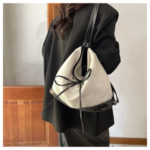 Canvas tote bag with black leather trim and bow detail shown on model's shoulder