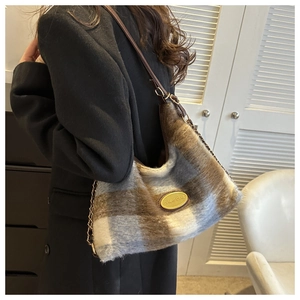 Detail of blue and brown plaid plush tote bag featuring a gold oval brand emblem