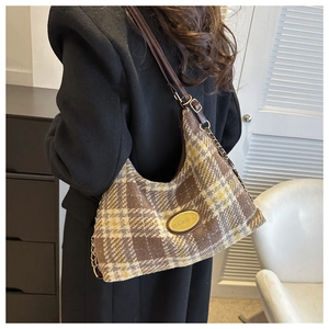 Detail of checkered plaid tote bag featuring a gold logo plate and leather chain strap
