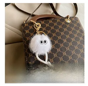 Close-up of a white plush cartoon charm with legs attached to a brown leather handbag