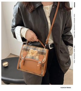 Detail of plaid crossbody bag featuring brown leather trim and a cute plush bear patch