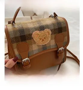 Detail of plaid wool fabric with a cute teddy bear patch and magnetic buckles on bag