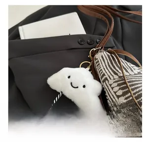 Close-up of white plush cloud bag charm with a smiley face and striped legs on a tote bag