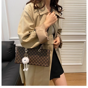 Détail du sac à bandoulière marron avec monogramme, chaîne dorée et charm en peluche