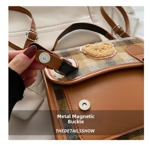 Detail view of the metal magnetic buckle on the brown checkered backpack with bear patch