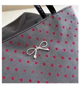 Close-up of gray tote bag with red hearts and silver bow charm detail on the front