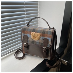 Detailed close-up of plaid wool fabric and plush bear patch on retro college bag