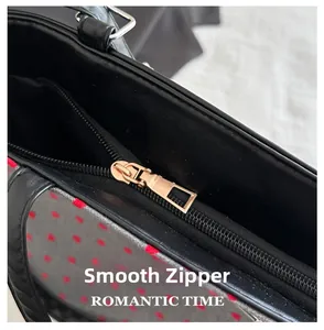 Close-up of smooth gold metal zipper closure on black and red polka dot tote bag