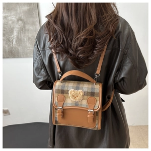 Detailed view of vintage plaid backpack with leather straps and plush bear patch on model