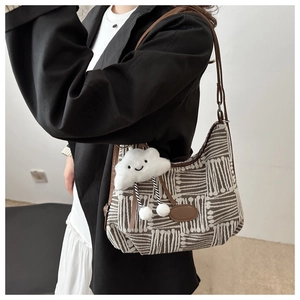 Detail of checkered canvas tote bag featuring brown leather straps and a plush cloud charm
