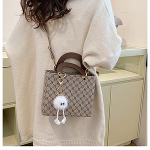 Close-up of monogram pattern tote bag with brown handles and white fuzzy monster charm