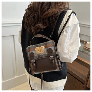 Detail of vintage plaid school bag featuring a golden plush bear patch and leather trim