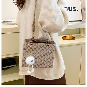 Detail of beige monogram tote bag with brown handles and a cute plush toy charm