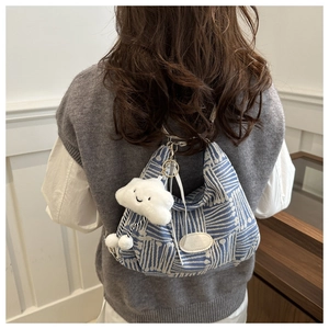 Detail of blue plaid canvas bag with leather patch and a white cloud plush charm