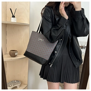 Mirror selfie of a gray heart-print tote bag with black straps and silver bow detail