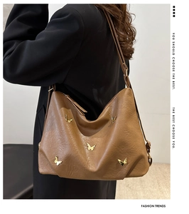 Detail of a brown pleated tote bag with golden butterfly charms on lychee texture leather