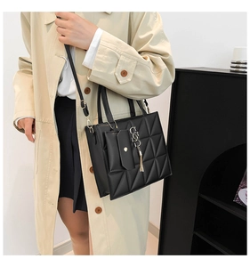 Dettaglio della borsa tote nera trapuntata con nappa e pochette indossata da modella