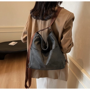 Macro shot of large black leather tote bag with brown fabric strap and side pocket detail
