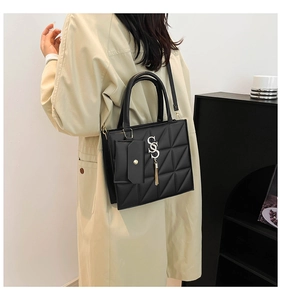 Quilted black crossbody bag with silver lettering and mini pouch worn over a beige coat