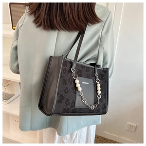 Detail of black tote bag with floral texture and elegant pearl metal chain strap
