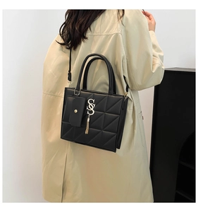 Dettaglio borsa trapuntata nera con ciondolo SSS dorato e tracolla su un trench beige