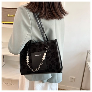 Detail of black textured tote bag featuring large pearl and floral metal chain straps