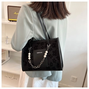 Detail of black tote with floral flocking patterns and a decorative pearl chain accessory