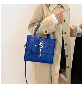 Detail of royal blue quilted handbag featuring metal initials and a tassel bag charm