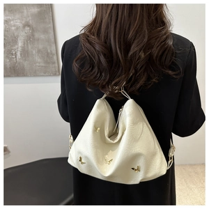 Detail of cream white tote bag with golden butterfly accent and elegant chain handle