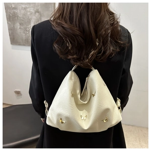 Detail of cream tote bag with gold butterfly accents worn by a model in a black suit