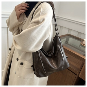 Dettaglio di borsa tote marrone scuro con cerniere argento su cappotto beige lana