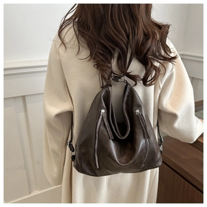 Detail view of the brown leather tote bag showing silver zippers and matte texture on model