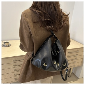 Detailed view of black pleated hobo bag with gold butterfly charms worn on shoulder