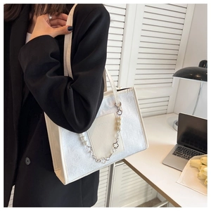 Detail of white jacquard tote bag with pearl chain and floral metal charms on shoulder