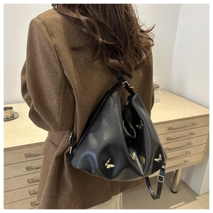 Detail of black half-moon shoulder bag with golden butterfly emblem on brown blazer