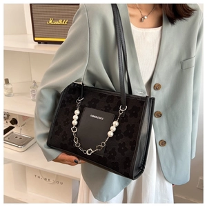 Detail of black floral tote bag with large white pearl chain on model shoulder