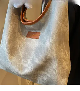 Close-up of grey washed canvas tote bag featuring brown leather handles and brand tag