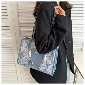 Close-up of light blue textured tote bag with elegant pearl chain and brand logo detail