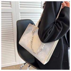 Close-up of cream white shoulder bag featuring floral embossing and pearl clover chain