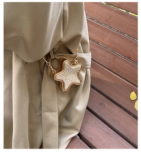 Dettaglio di una borsa a tracolla dorata a forma di stella con strass su un trench