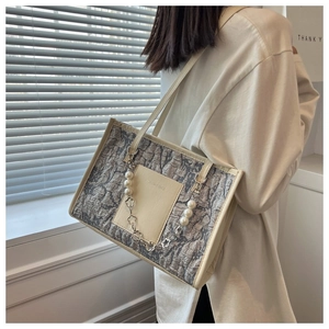 Detail of minimalist tote bag featuring textured fabric and pearl floral chain accessory